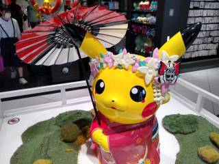 Geisha Pikachu greets you! A statue of Pikachu, dressed in a dark pink kimono, wearing a flower crown and carrying a parasol.