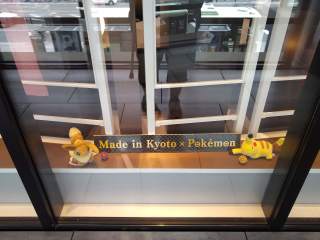 Proof of Kyoto Pokemon Center Between two small plush Pokemon, a sign saying 'Made in Kyoto x Pokemon'