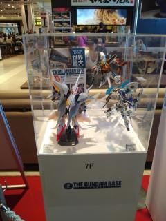 A few Gundam toys for advertisement A glass case containing three small Gundam toys, and a flyer for The Gundam Base.