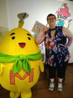 Thia with the Manga Museum mascot Thia standing next to a full-size, fabric model of Mamyu, the bright yellow Manga Museum mascot